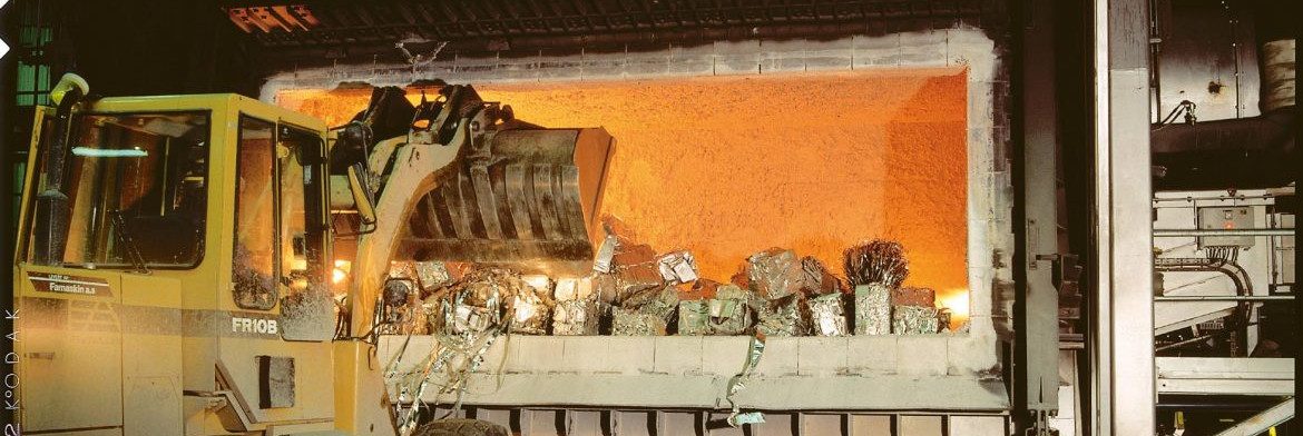The Aluminum Association. A bucket loader dumping aluminum into a furnace with other visible metal.