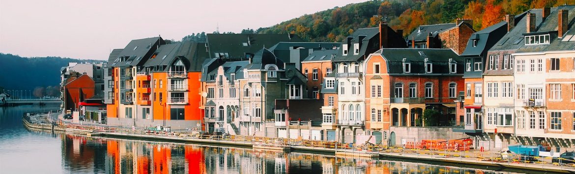 A row of multistory buildings along the water with a mountain behind.